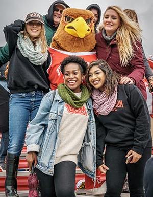 Female Montclair State University students posing with Rocky at Homecoming.