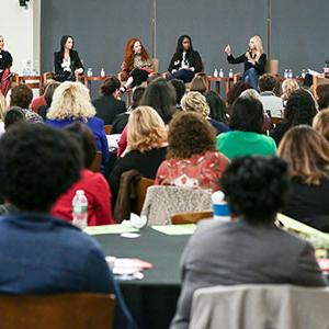 A panel of female entrepreneurs speaking in front of crowd.