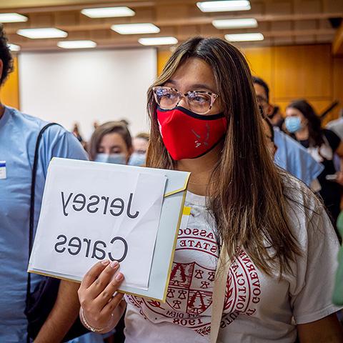 student wearing mask holding "Jersey Cares" sign