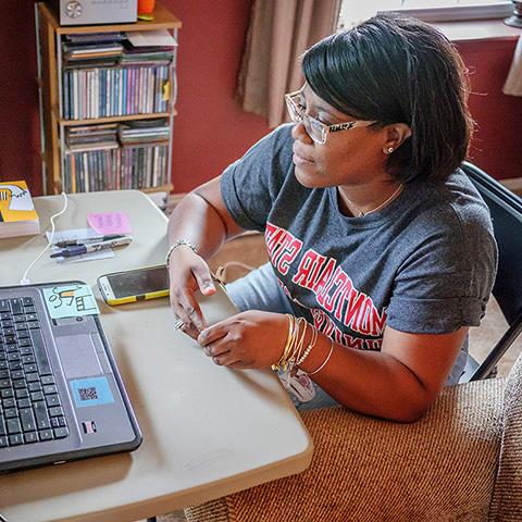 student wearing Montclair State University t-shirt sitting with laptop