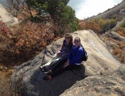 Two girls sitting on a rock at an overlook on a sunny day