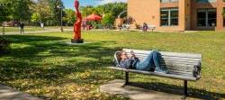 Student in outside of Dickson hall lying on bench