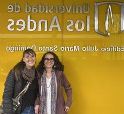 two women standing and smiling in front of building signage