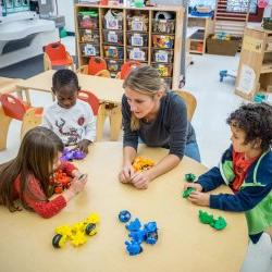 Photo of teacher with young children and blocks in classroom.