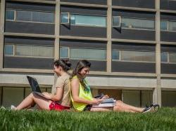 两个学生背靠背坐在布兰顿大厅外的草地上.