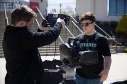 Two college students standing outside holding and testing broadcast equipment